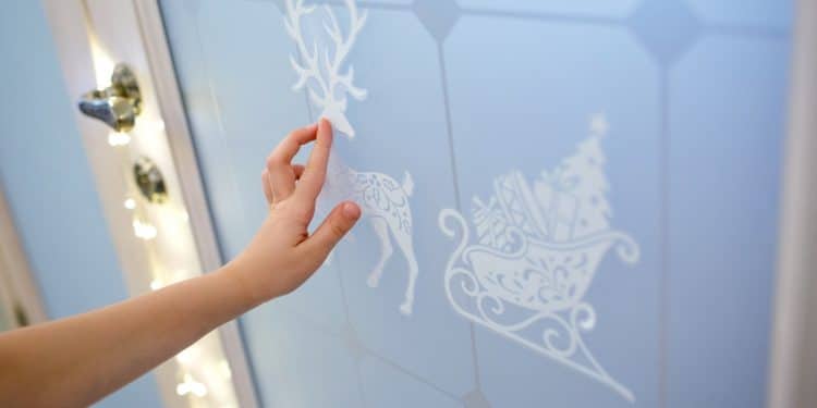 Kid's hand touching white Christmas reindeer sticker on the door.