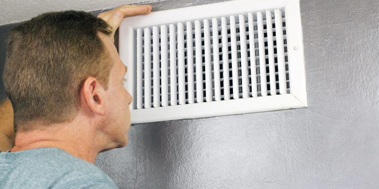 Mature man examining an outflow air vent grid and duct to see if it needs cleaning. One guy looking into a home air duct to see how clean and healthy it is.