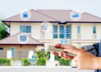 Hand using smart phone as smart home control application over blurred house background, smart home concept