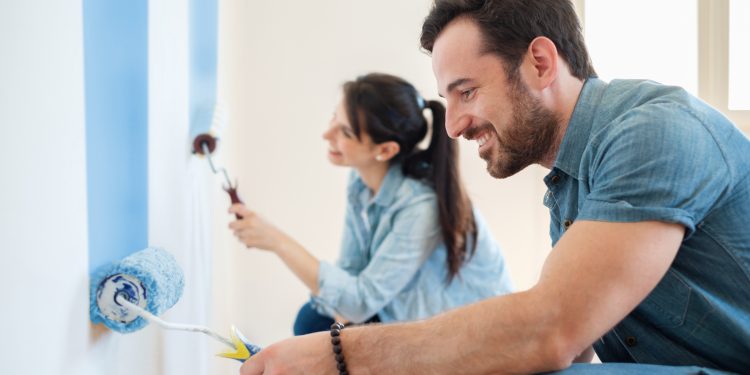 Young couple painting walls in their new house, do it yourself concept