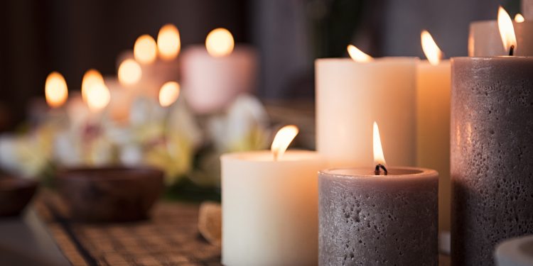 Closeup of burning candles spreading aroma on table in a spa room. Beautiful composition with grey and white candles for spa treatment. Zen and relax concept.