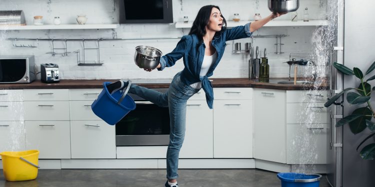 Full length view of shoked woman in jeans dealing with water leak in kitchen