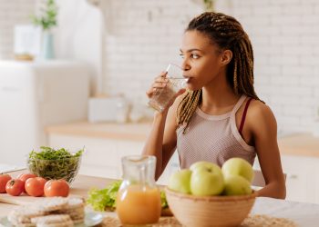 Water before breakfast. Slim and fit woman with many little braids drinking water before having breakfast