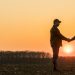 Two farmers on the field shake hands at sunset.