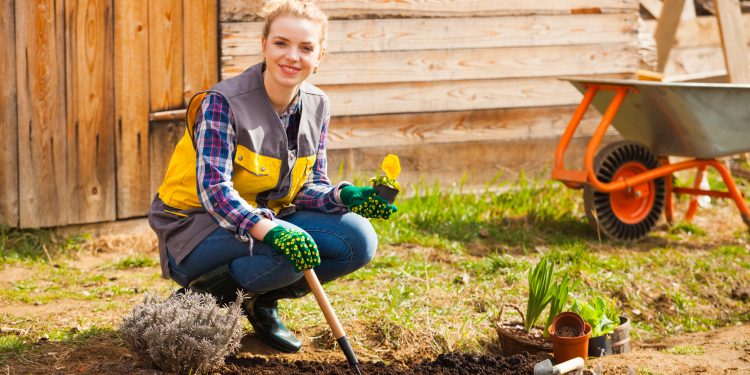 Attractive young blond woman sitting,working in her garden. Uniform, gloves, garden tools