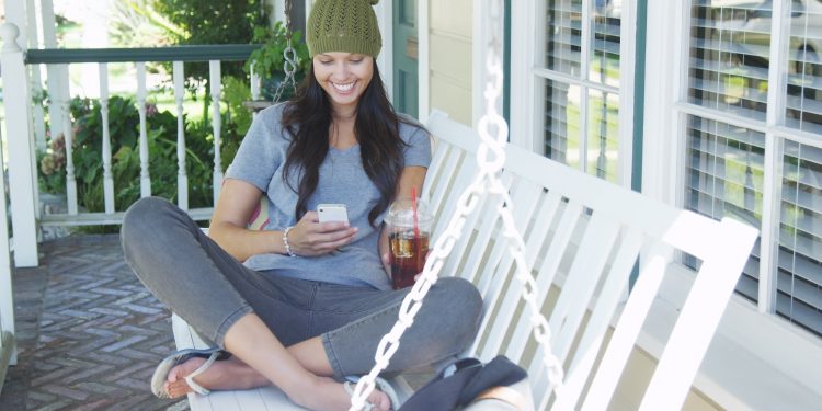 Young woman texting and sitting on porch