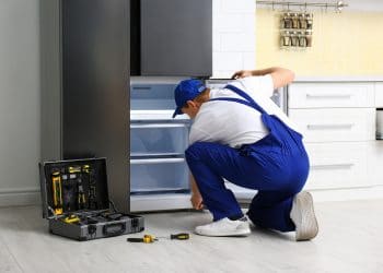 Male technician repairing broken refrigerator in kitchen