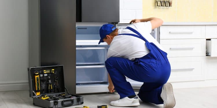 Male technician repairing broken refrigerator in kitchen