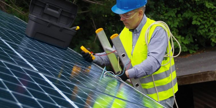 A person wearing a hard hat and safety vest working on a solar panel Description automatically generated with low confidence