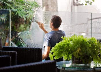 Man in Gray Shirt Cleaning Clear Glass Wall Near Sofa