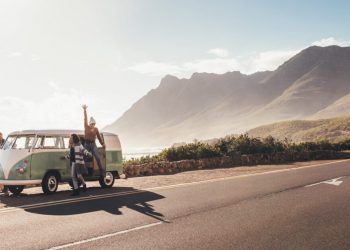 Friends on road trip on a sunny day. Group of man and women hangout by the road with old minivan.