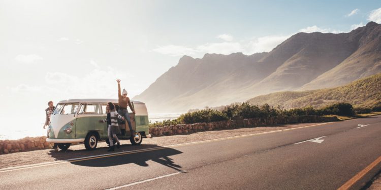 Friends on road trip on a sunny day. Group of man and women hangout by the road with old minivan.