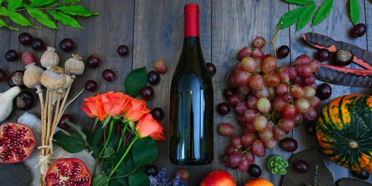 Wine Bottle Beside Grapes, Roses and Several Fruits on Brown Wooden Surface