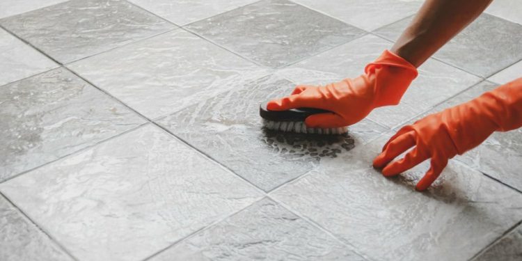 Hand of man wearing orange rubber gloves is used to convert scrub cleaning on the tile floor.