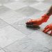 Hand of man wearing orange rubber gloves is used to convert scrub cleaning on the tile floor.