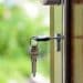 a bunch of keys dangling as one of these bunch is lodged into an open door with greenery in the background.