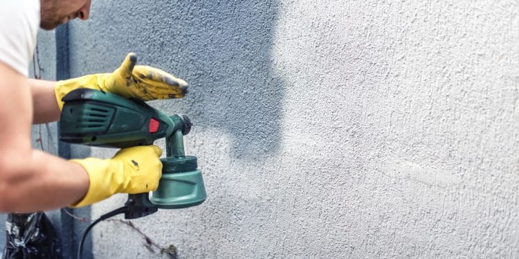 Man painting a grey wall, renovating exterior walls of new house